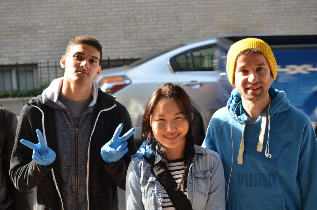 DSC_7243 Three friends smiling outdoors, one in gloves making peace signs, casual and happy vibe.