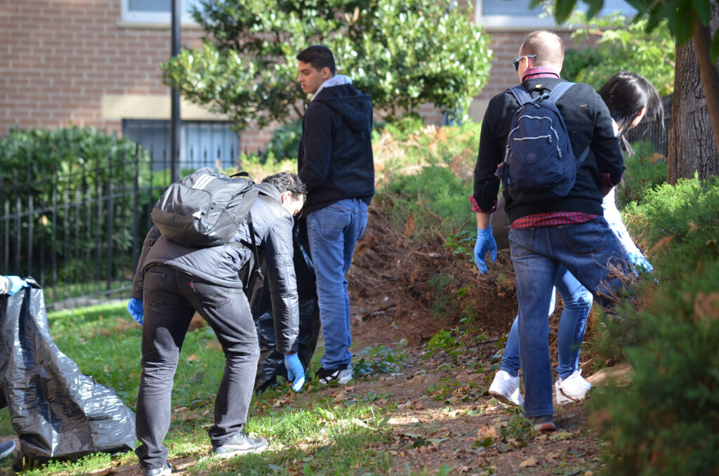 DSC_7252 Volunteers cleaning a park, picking up trash, and wearing gloves and backpacks, outdoors on a sunny day.