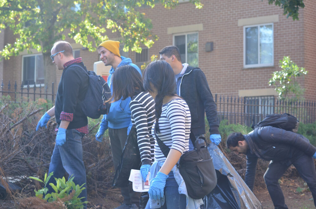 DSC_7256 Volunteers cleaning up outdoors, wearing gloves and casual clothes, near residential buildings.