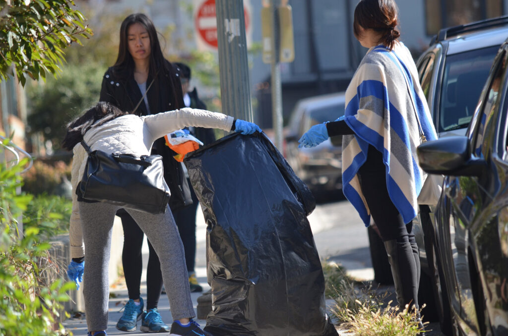 DSC_7294 Volunteers cleaning up a neighborhood street, placing trash in large black bags, showcasing community spirit.