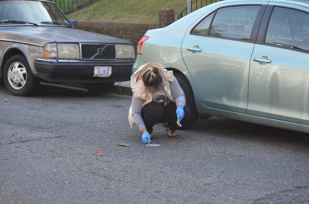 DSC_7300 Person cleaning street next to parked cars wearing blue gloves.