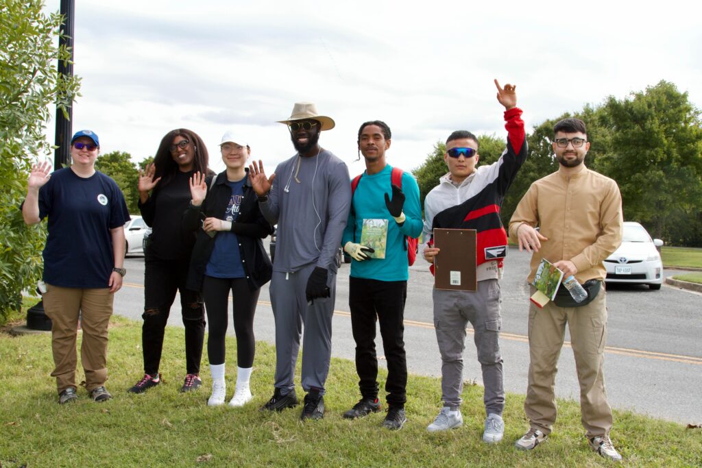 IMG_2858 Group of diverse people standing together outdoors, waving and smiling, engaged in a community event.