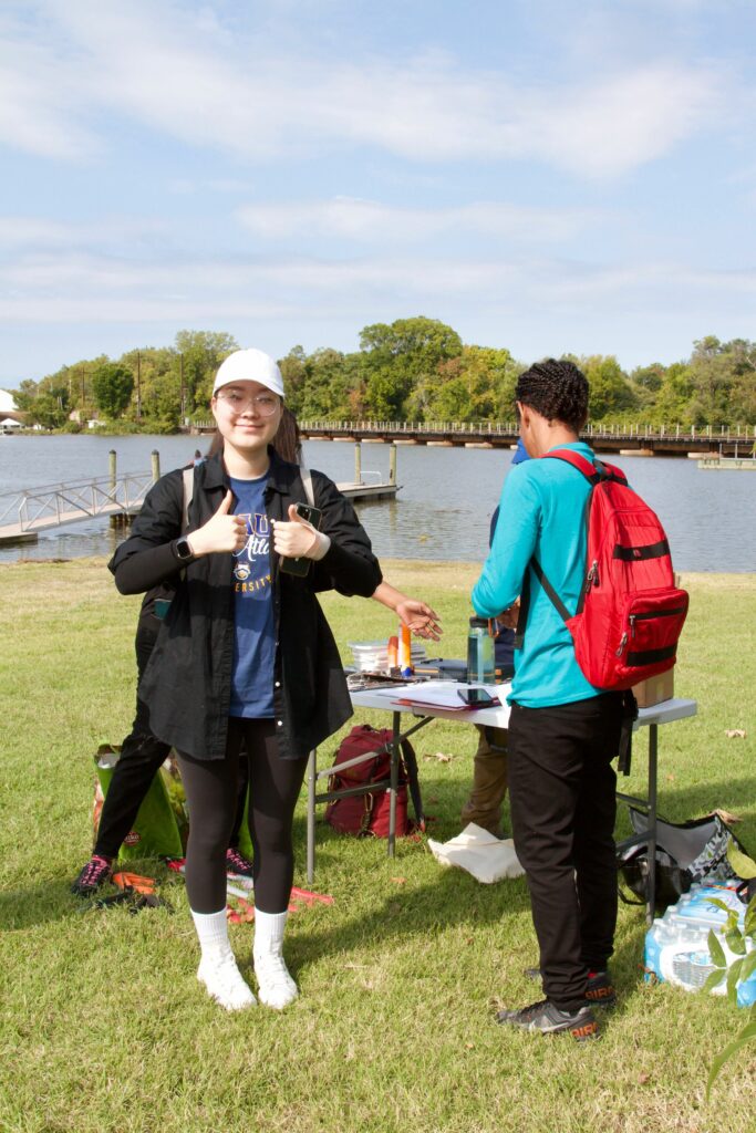 IMG_2868 Outdoor event by a lake with people socializing and setting up tables under a clear sky.