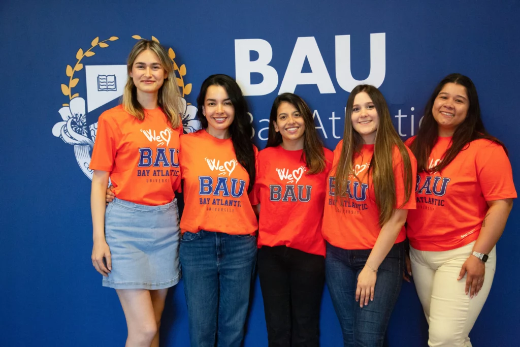 Group of women in orange We Love BAU shirts smiling at Bay Atlantic University event.