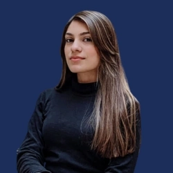 Portrait of a woman in a black sweater against a blue background, looking confidently at the camera.