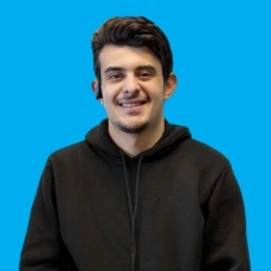 Smiling person in a black hoodie with blue background, wearing an earpiece, looking at the camera.