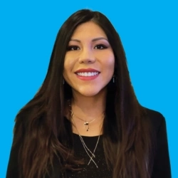 Smiling woman with long hair against a bright blue background, wearing a black outfit and layered necklaces.