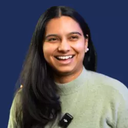 Smiling person with long hair, wearing a microphone, against a blue background.