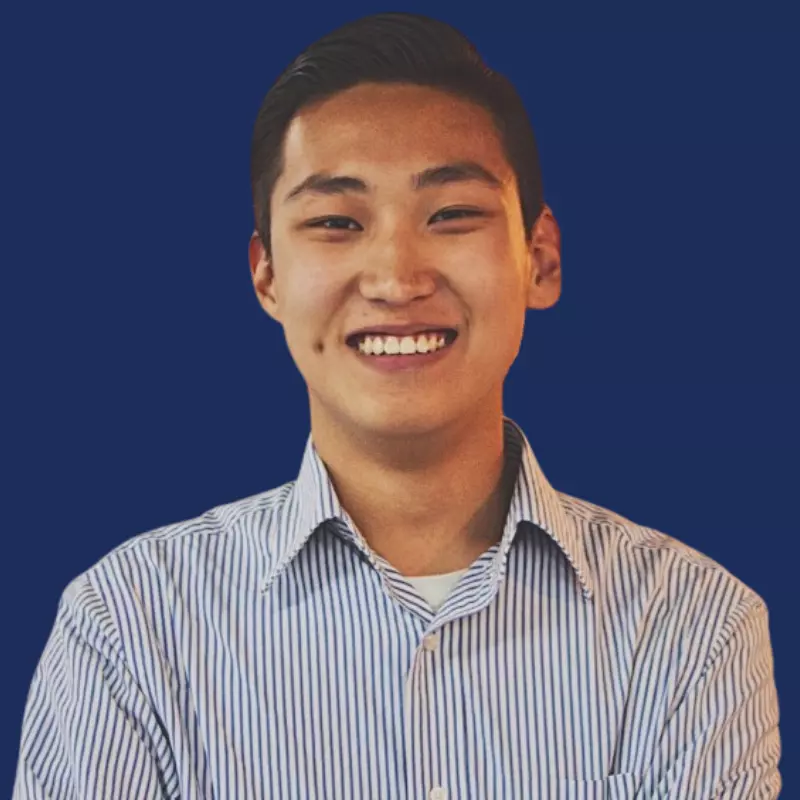 Smiling person in a striped shirt with a blue background, arms crossed, friendly expression.