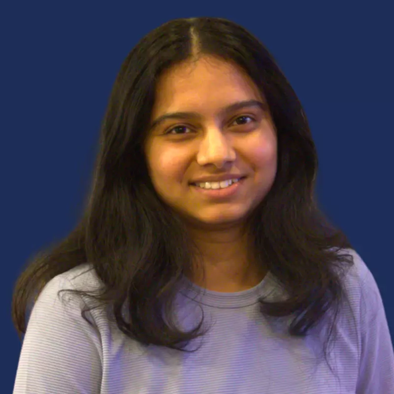 Smiling person with long hair and blue shirt against a plain blue background.