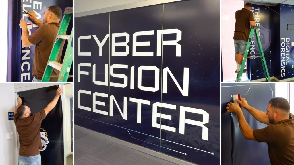 Man installing wall graphics at Cyber Fusion Center with digital forensics and threat intelligence displays.
