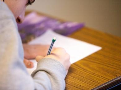 Average ACT Score for 2023: What Is It and How to Improve 47 Student writing on paper with pencil at a wooden desk, focused on an assignment.