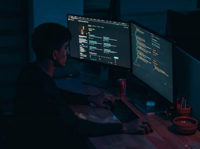 How to Become a Cyber Security Analyst: Guide for 2025 6 Developer coding at night on dual monitors with a drink on the desk.