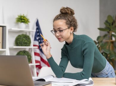 How to Learn English: Simple Tips for Effective Learning 21 Young woman studying with laptop and books, American flag in background, office setting.