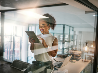 Confident businesswoman smiling while using a tablet in a modern office setting, showcasing results of soft skills in tech jobs