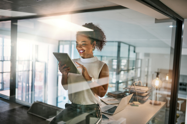 Confident businesswoman smiling while using a tablet in a modern office setting, showcasing results of soft skills in tech jobs