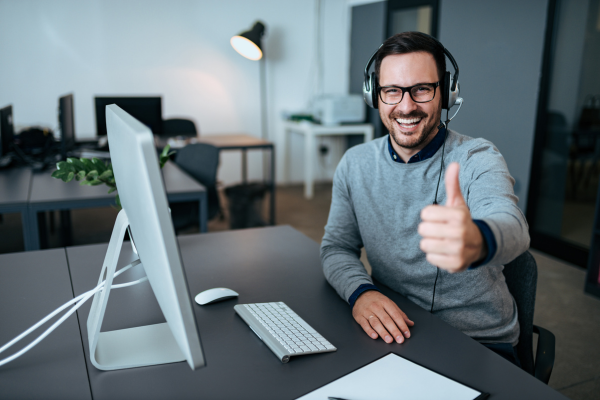Cheerful customer support agent giving a thumbs-up at his computer, reflecting positive attitude and interpersonal soft skills in tech jobs