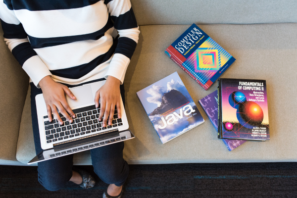 Person studying computer science and AI with books on Java, computer design, and a laptop — AI education and coding skills concept.