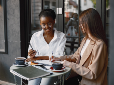 Two professional women collaborating over coffee at an outdoor café, discussing career strategies and professional growth opportunities.