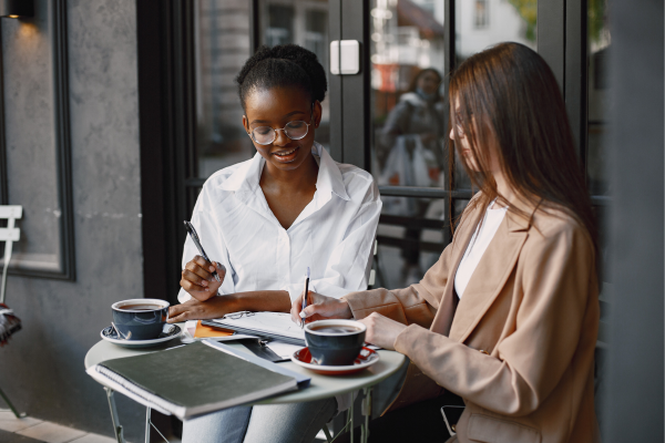 Two professional women collaborating over coffee at an outdoor café, discussing career strategies and professional growth opportunities.