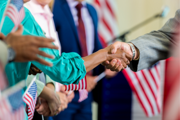 Diverse group shaking hands at a patriotic event with American flags in the background.