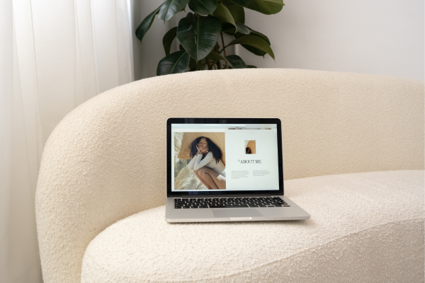 Laptop on a modern sofa displaying a personal website with an About Me page focused on personal branding. 