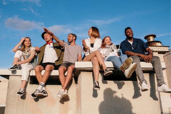 A group of friends sitting and laughing on a rooftop under a clear blue sky, enjoying a sunny day.