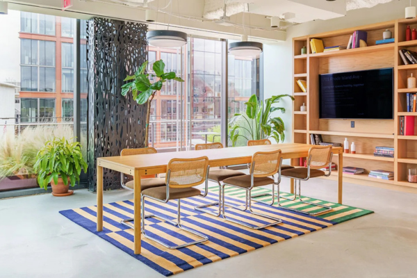 Bright and modern study space at a WeWork location in Washington, D.C., featuring a wooden table, bookshelf, indoor plants, and city views. Photographs by WeWork.