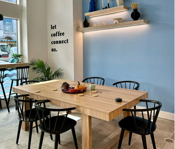 Modern cafe interior with wooden table, black chairs, and a welcoming let coffee connect us sign on the wall.