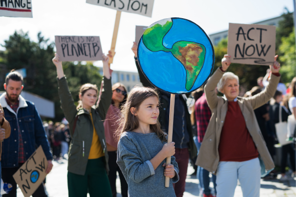Young girl holding Earth sign at a climate change protest, surrounded by activists with various environmental messages.