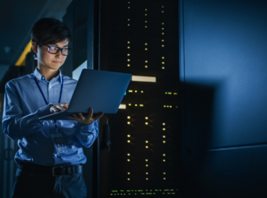 What Employers Look for in Cybersecurity Graduates Today 15 cybersecurity graduates works on a laptop in a dimly lit server room, managing network hardware and data security.