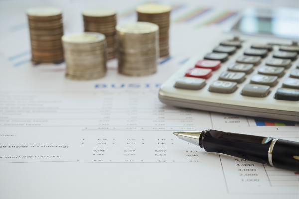 Calculator, pen, and coin stacks on financial documents, emphasizing budgeting and financial planning concepts.