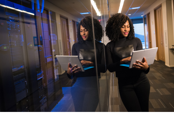 Woman using laptop in server room, reflecting on glass wall, enhancing cybersecurity and technology efficiency.