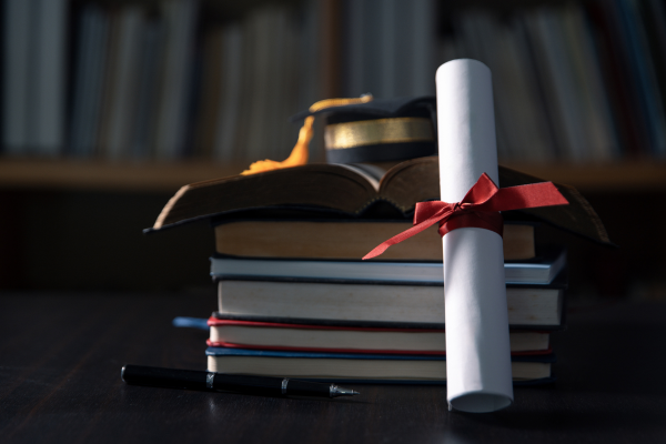 Graduation cap and diploma on stacked books, symbolizing academic achievement and education success.