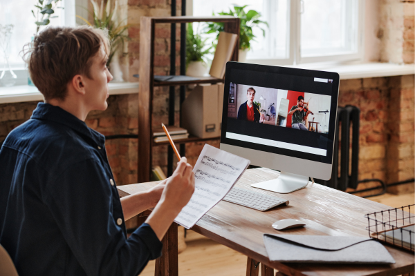 Person reviewing music notes while attending an online video meeting with musicians on a computer screen.