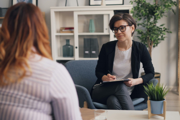 Therapist and client in a counseling session, sitting in a cozy office setting with plants and shelves in the background.