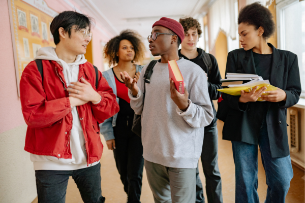Group of diverse students talking and holding books in a school hallway.