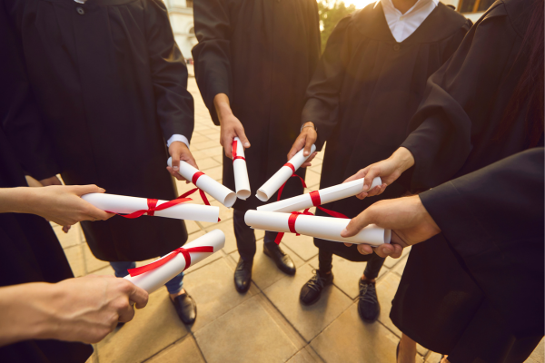 Graduates in caps and gowns holding diplomas celebrate on graduation day outdoors.