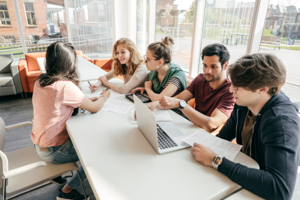 Group of young adults collaborating at a table with documents and a laptop in a bright room.