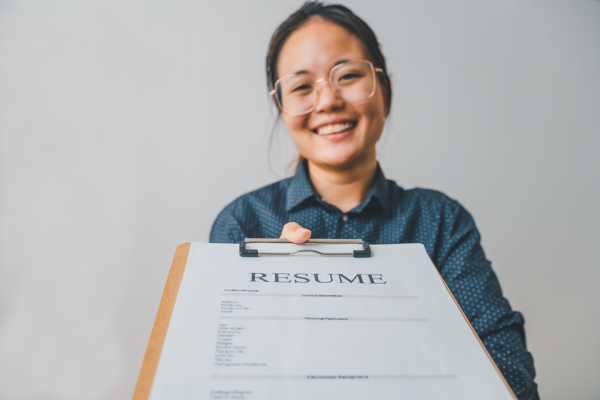 Smiling person presenting a resume on a clipboard, highlighting career readiness and job application process.