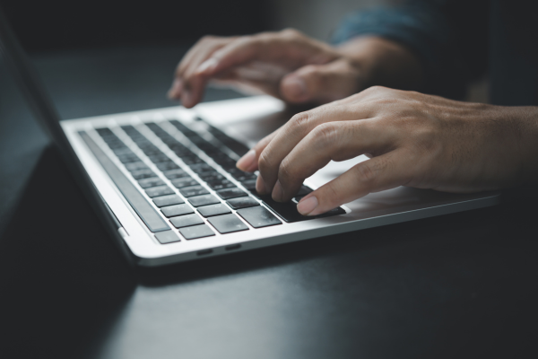 Hands typing on a laptop keyboard, close-up on dark desk, illustrating modern business and technology