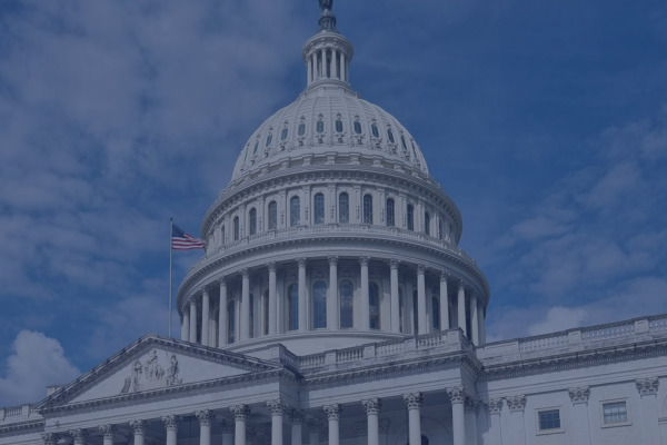 U.S. Capitol Building under blue sky, American flag waving, symbol of government and democracy.