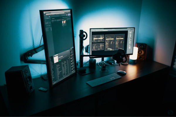 Modern dual-monitor workspace with headphones and speakers in dim lighting.