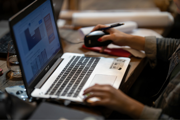 Person using a laptop and mouse at a wooden desk, working or browsing online.