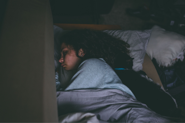 Woman sleeping peacefully in bed with a black cat cuddled beside her under a cozy blanket.