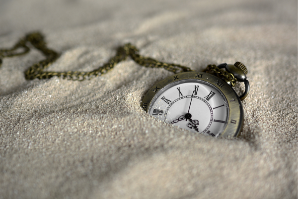 Vintage pocket watch partially buried in sand, symbolizing the passage of time and timeless elegance.