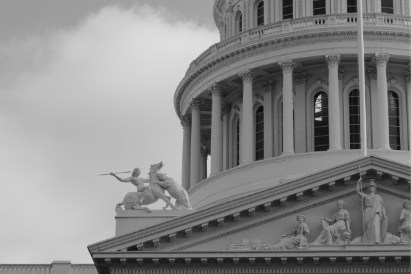 Black and white image of a classical building facade with statues and columns under a partly cloudy sky.