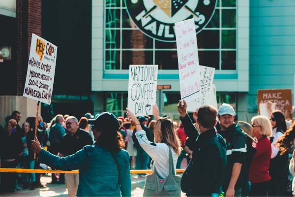People holding protest and National Coffee Day signs in front of a building during a public demonstration.