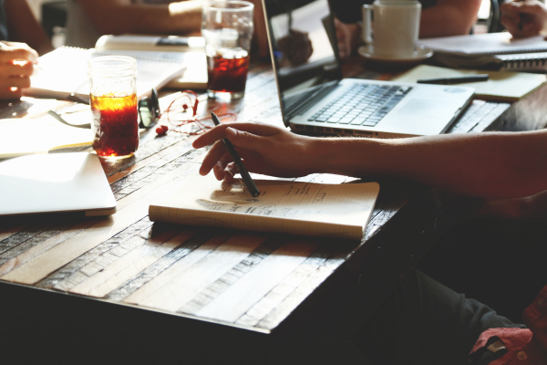 A person engaged in lifelong learning, writing notes on paper while studying in a coffee shop.