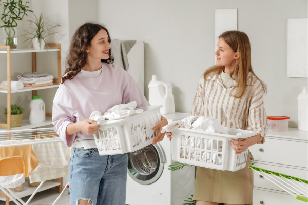 On-Campus vs Off-Campus: Best Housing for International Students 9 Two international students carrying laundry baskets and chatting in a shared apartment, illustrating everyday life in housing for international students.